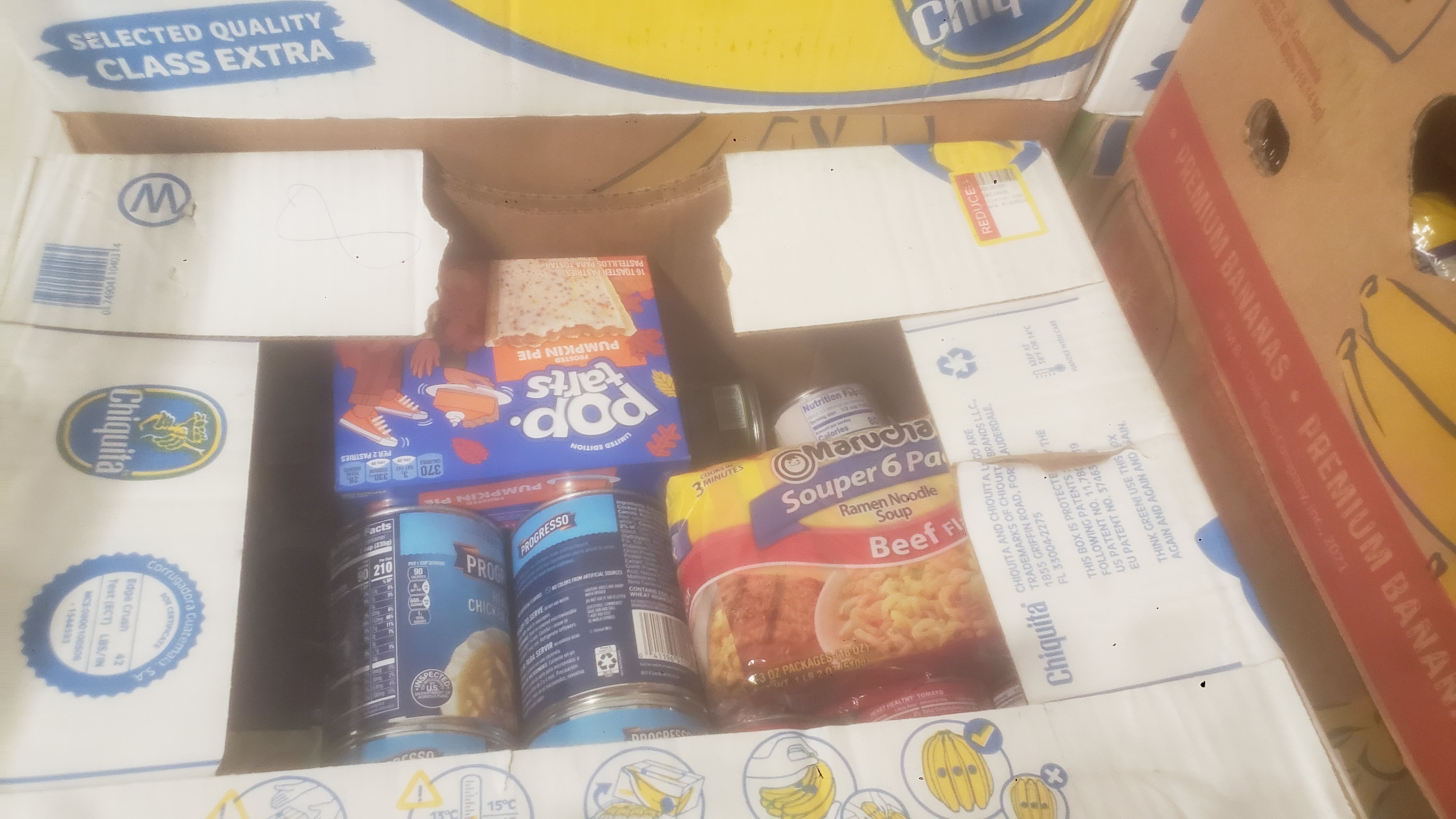 Emergency food banana box with a pack of ramen, box of pop tarts, and two cans of soup showing on top.